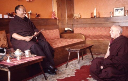 Venerable Kechog Palmo sitting on the floor, smiling, looking at Rangjung Rigpe Dorje, also smiling.