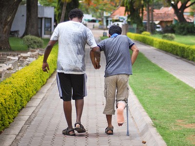 Man helping another young man with a crutch.