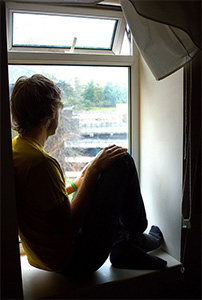 Young man sitting on window sill, staring out window.