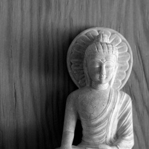 A white stone statute of buddha with wood background.