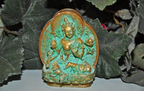 Green Tara tsa tsa with gold trim in front of leaves.