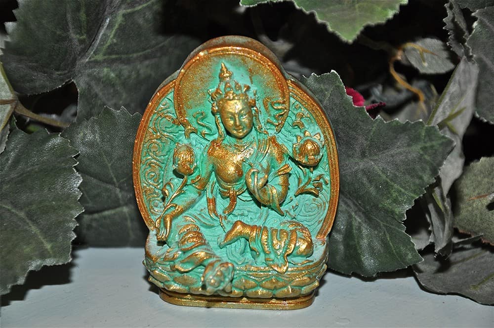 Green Tara tsa tsa with gold trim in front of leaves.