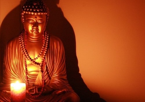 Statute of a buddha and a candle light shining in front of the buddha.