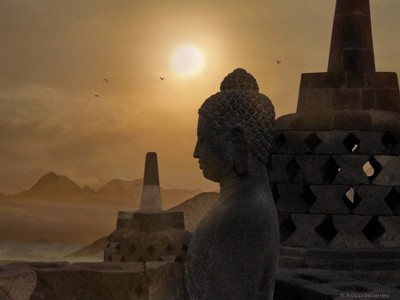 Buddha statute at Borobudur with the sun in the background.