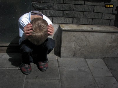 A boy squatting down with his hands covering his head.