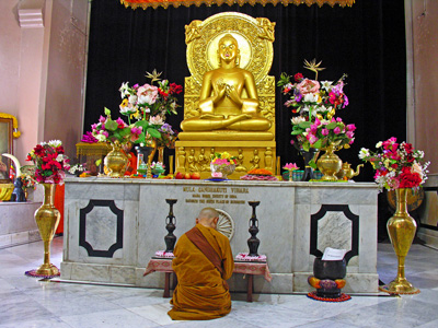 A bhikkhuni kneeling into front of a buddha statue praying.