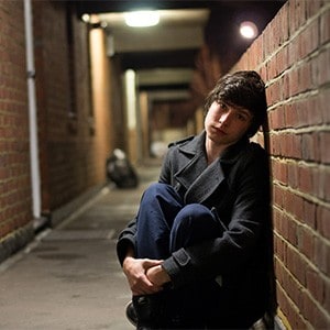 Young woman sitting alone, leaning against a wall.