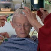 Venerable Samten with eyes closed while two nuns shave her head.