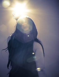 The back view of a woman stretch her hand trying to catch light in front of her.