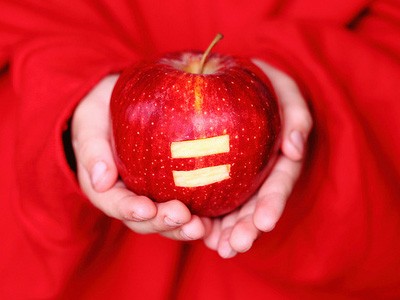 Child holding an apple with an equal sign carved into it.