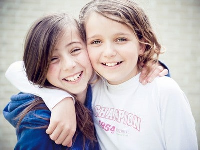 2 young girls putting their hand on each other shoulder and smiling happily.