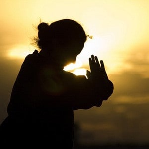 A woman putting her hands in praying position, sunset in the background.