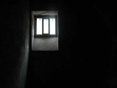 Prison cell window that has light pentrating through, surroundings are in darkness.