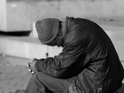 A sad man sitting in the street, head bowing low.