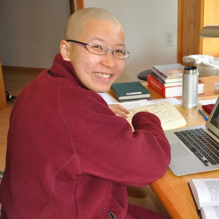 enerable Damcho smiling, with a book and laptop.