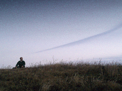 Man sitting outside in field under clear sky at dusk.
