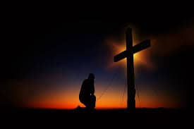 Man kneeling before a cross and sunset