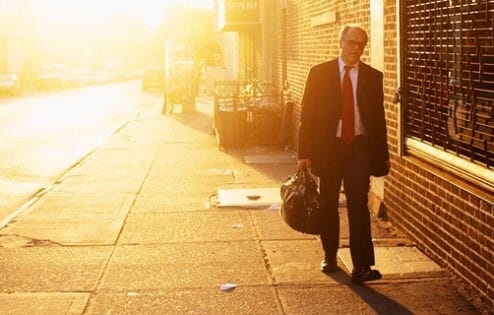 Man in business suit and carrying briefcase, walking at sunset.