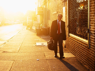 Man in business suit and carrying briefcase, walking at sunset.