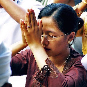 Woman with palms together and eyes closed.