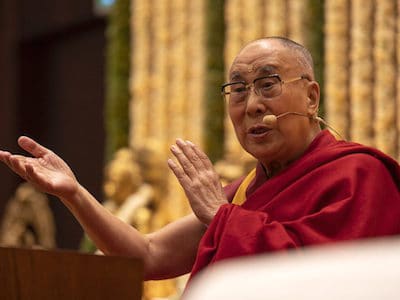 His Holiness teaching with arms raised.