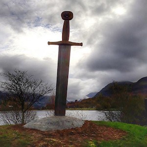 Sword sticking out of ground with pond in background.