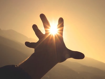 Silhouette of hand reaching out toward the sun.