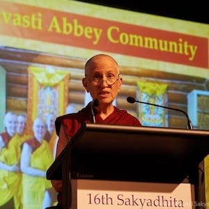 Venerable standing behind a podium with a photograph of the Sravasti Abbey community projected behind her.