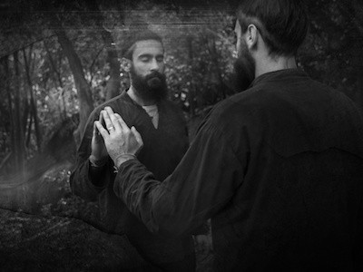 Black and white image of man with eyes closed, touching reflection in mirror.