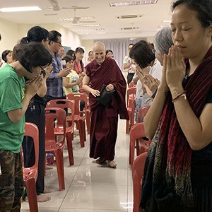 Venerable surrounded by people, smiling while walking toward the altar to teach.