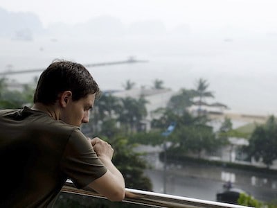 Man leaning over balcony railing, in contemplation.