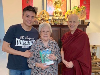 Kenryuu with his arm around his mother, both smiling and standing with Venerable Chodron.