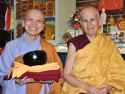 Venerable Pende standing next to Venerable Chodron, holding her robes and smiling.