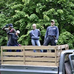 Young Adult Week participants stand and pose in the back of a truck in their work clothes.