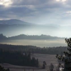 Meadow and hills beneath a misty cloudy sky.