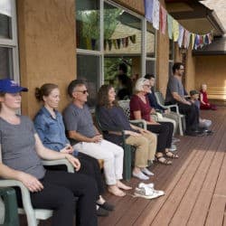 A row of people sit in meditation on chairs on the Chenrezig Hall deck.