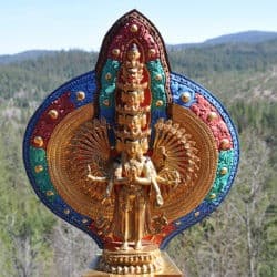 Statue of Thousand-Armed Chenrezig overlooking a meadow.