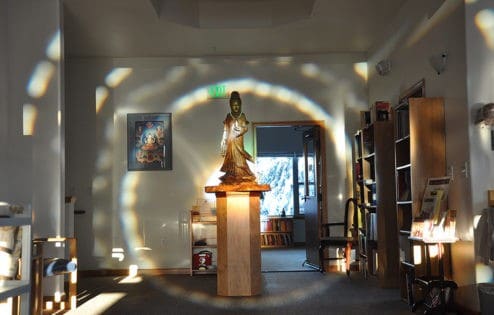 Wooden Kuan Yin statue on a pedestal with an aura of light around it.