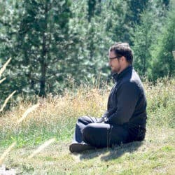 A man sits in meditation in a meadow.