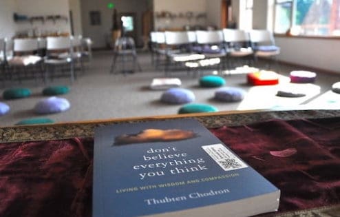 A copy of the book "Don't Believe Everything You Think" on the teacher's table facing a room with meditation cushions.