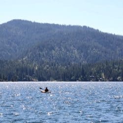 A solo person kayaks in a lake with mountains in the background.