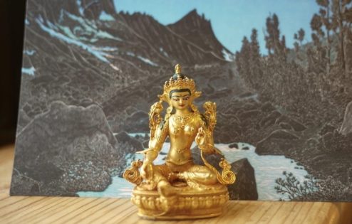 Golden Tara statue in front of a card showing a river and mountains.