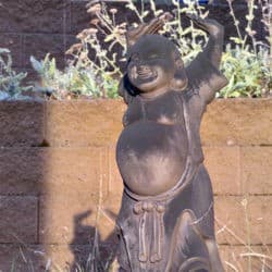 A statue of Maitreya Buddha with hands raised and laughing in the sun.