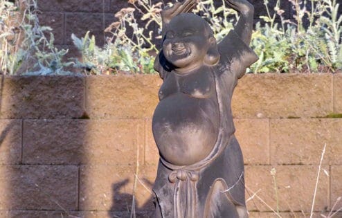 A statue of Maitreya Buddha with hands raised and laughing in the sun.