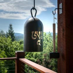 Bell with om symbol and its striker hanging on a deck overlooking landscape.