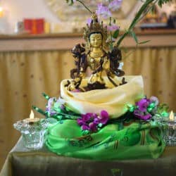 Bronze statue of tara wrapped in a thangka with flower and light offerings.