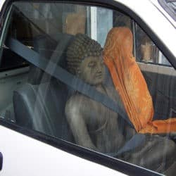 A buddha statue strapped in by a seat belt in the front passenger seat of a car.