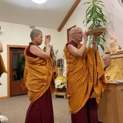 A line of three monastics carry offerings as part of the Lama Chopa Guru Puja.