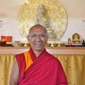 Geshe Dadul Namgyal stands in front of the Buddha on the altar.