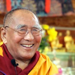 Geshe Lhundup Sopa smiles at the camera sitting in front of an altar.